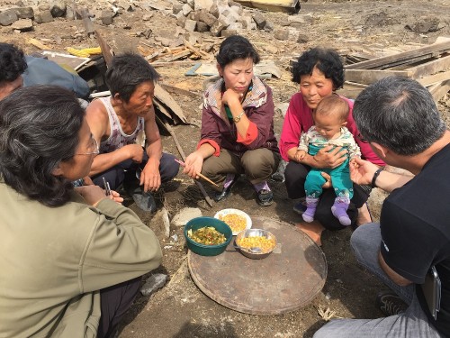 水害で破壊された家の残骸の上で食事を取る被災者（画像：UNICEF）