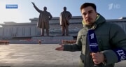 金日成、金正日銅像の前でレポートするロシアのチャンネル1のゲンナジー・カルチェリョフ記者（画像：同局Rutubeキャプチャー）